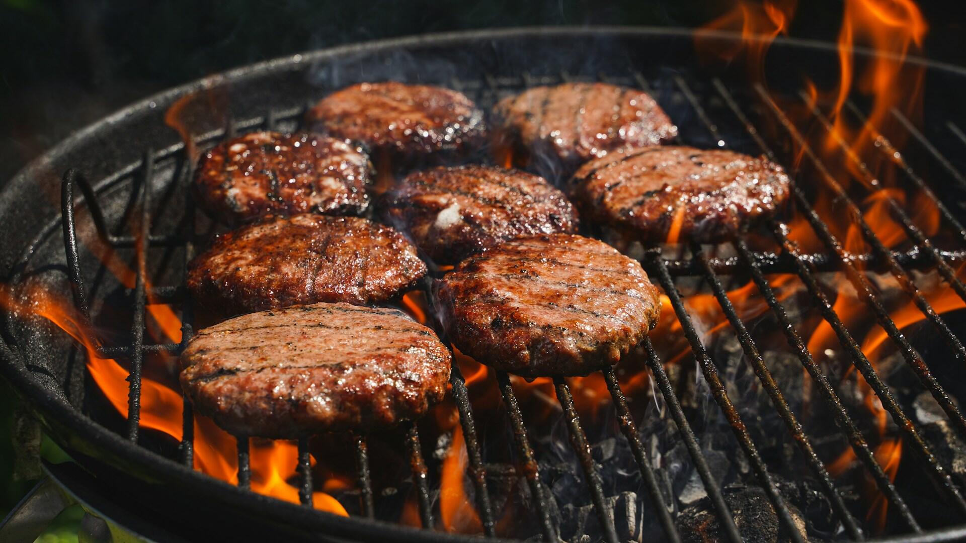 Hamburgere grilles på kullgrill over åpne flammer og glødende kull.