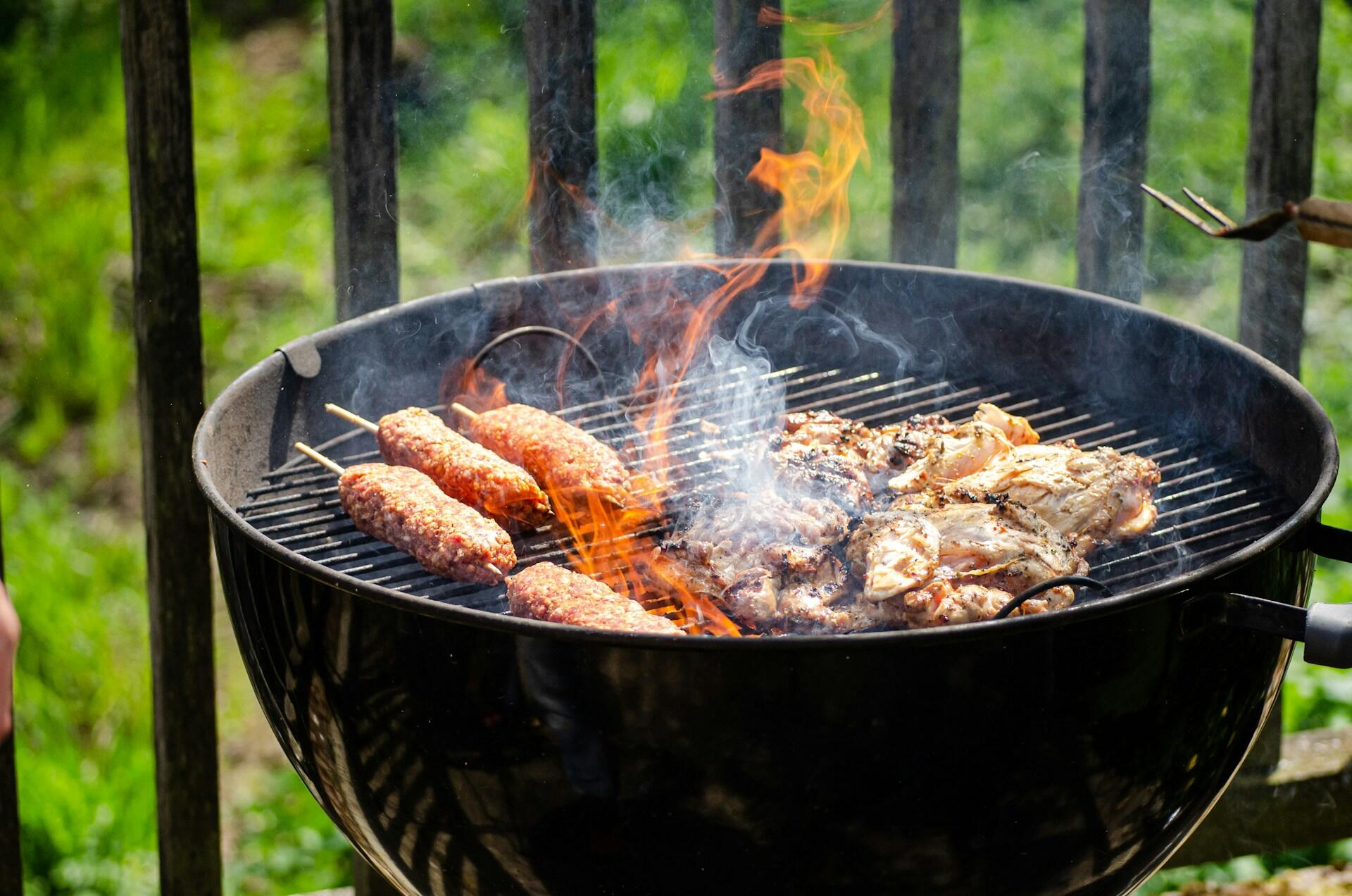 Kullgrill med kjøtt på grillspyd og kylling over flammer og røyk i en grønn hage.