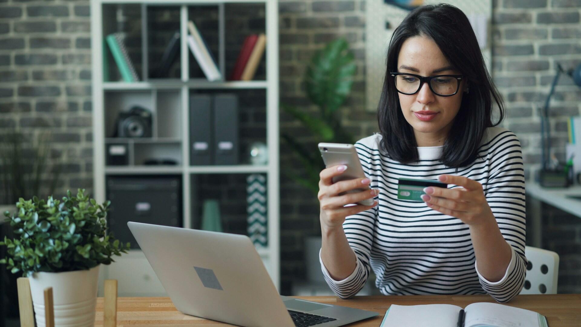 Person bruker mobil og bankkort ved en datamaskin