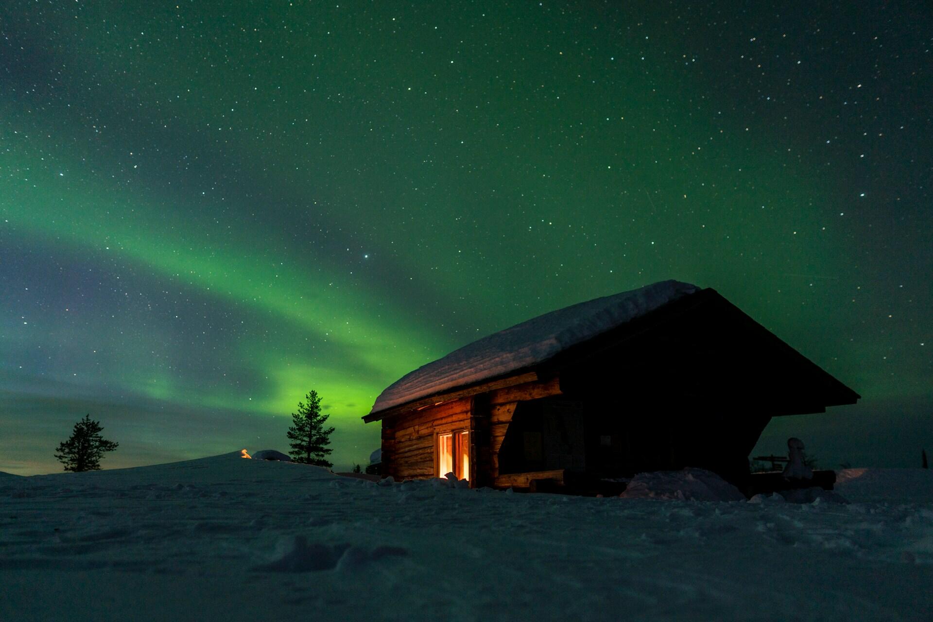 Nordlys på stjernehimmelen over en hytte i et snødekt landskap.