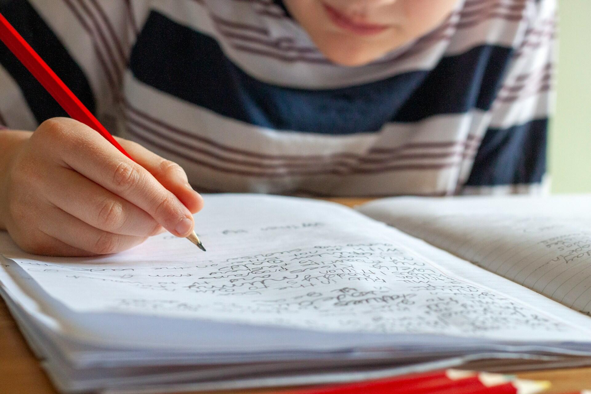 gutt som skriver lekser i notatbok hjemme, et av flere argumenter for lekser