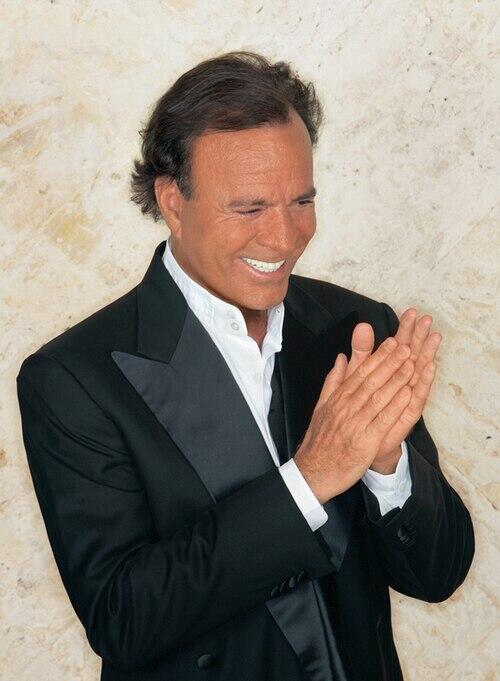 Den spanske sangeren Julio Iglesias smiler og applauderer i mørk dress.
