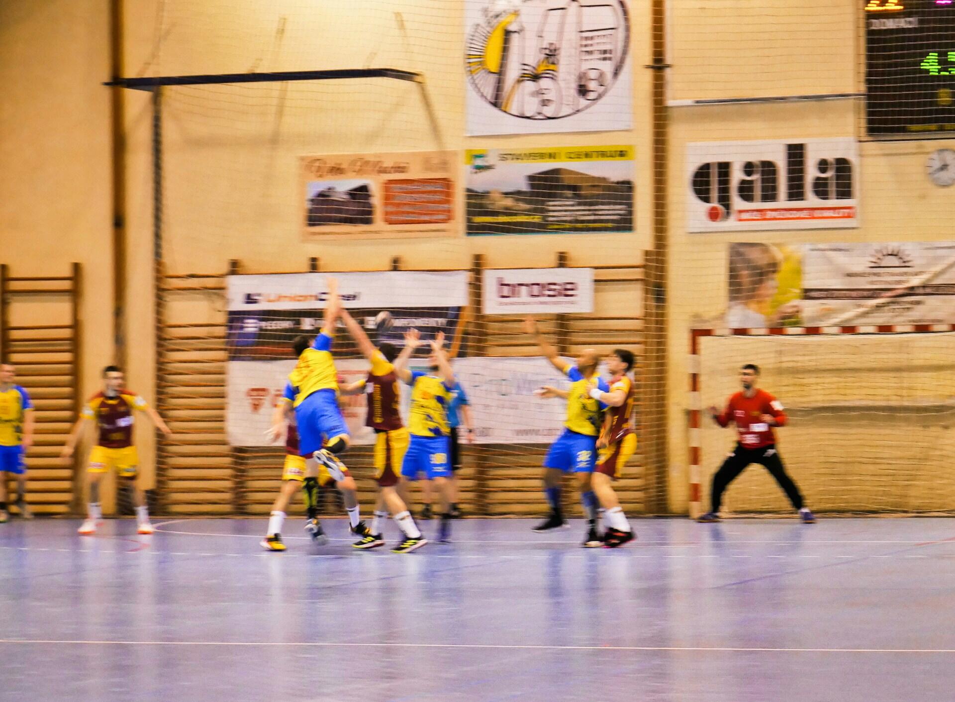 Håndballspillere i kamp foran mål i en idrettshall.