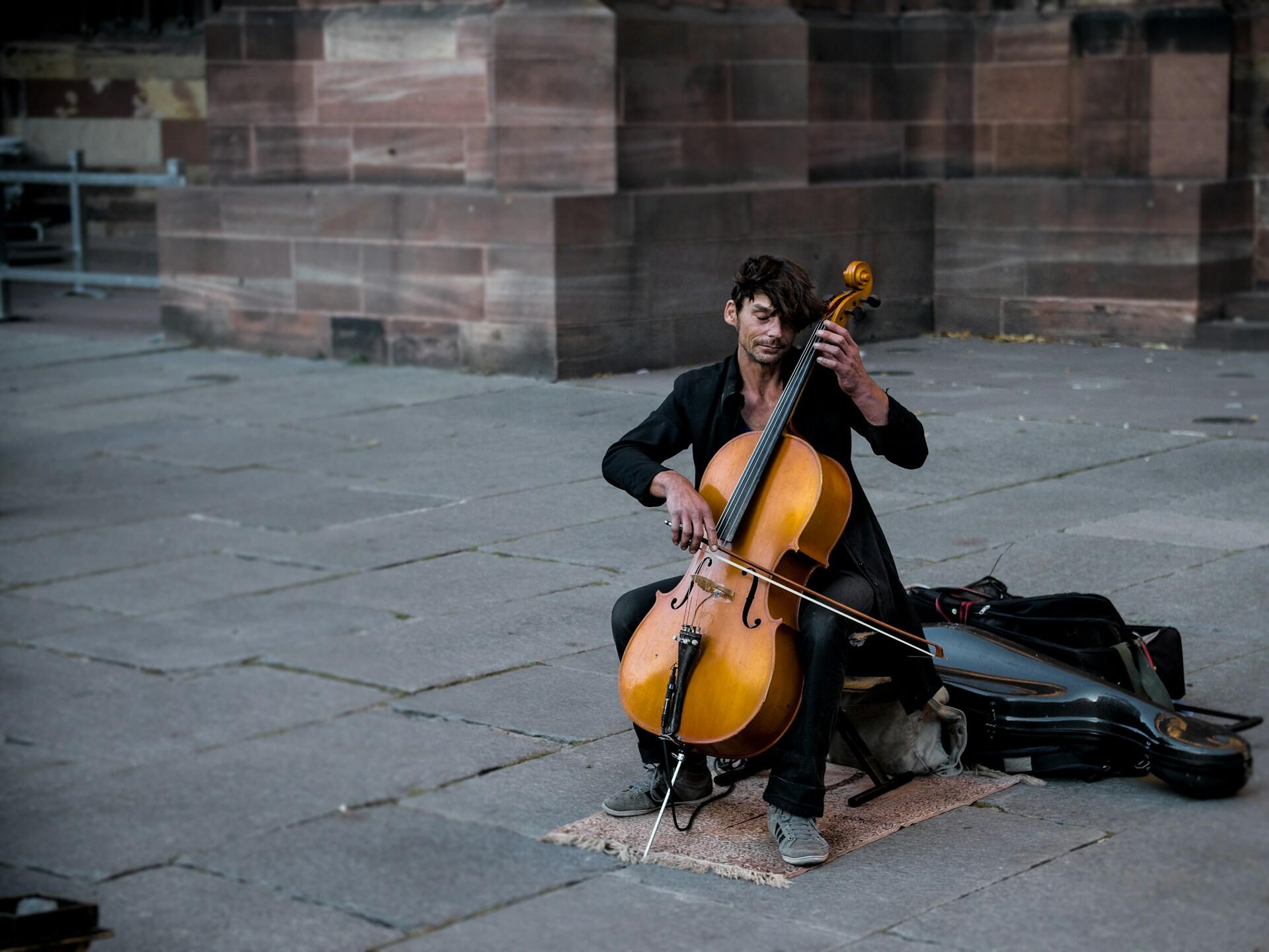 Gatemusikant sitter utendørs og spiller cello med bue