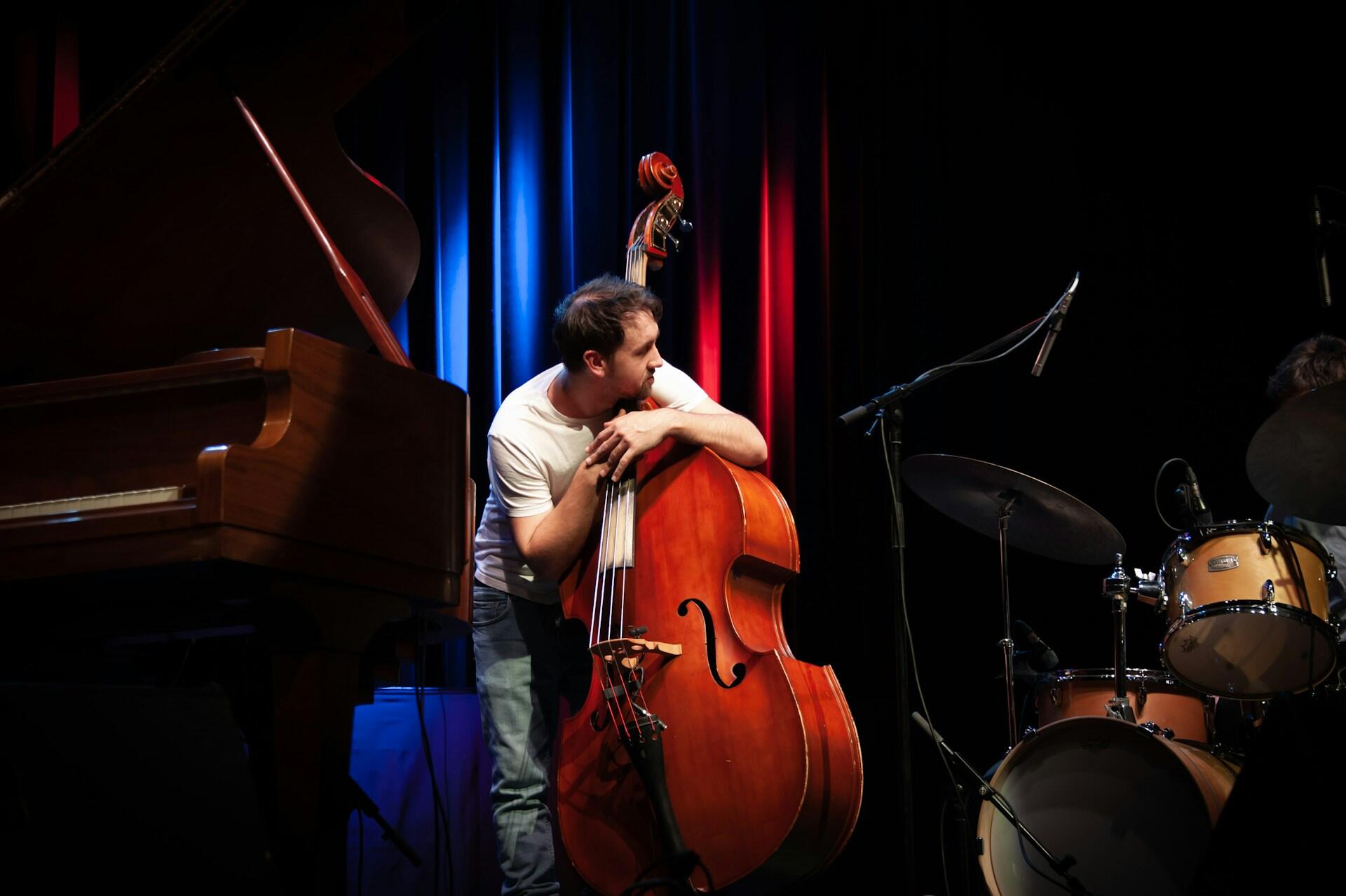 Mann holder en kontrabass på en scene med piano og trommer