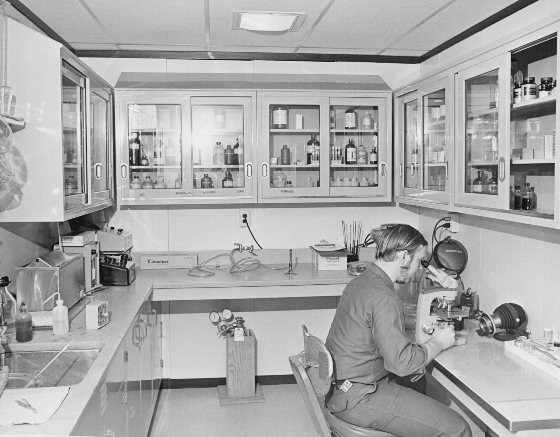 Forsker undersøker en prøve med mikroskop i et eldre laboratorium.