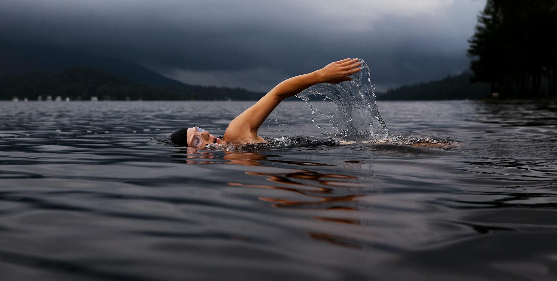 Person med badehette og svømmebriller svømmer crawl i åpent vann, et eksempel på svømming som treningsform.