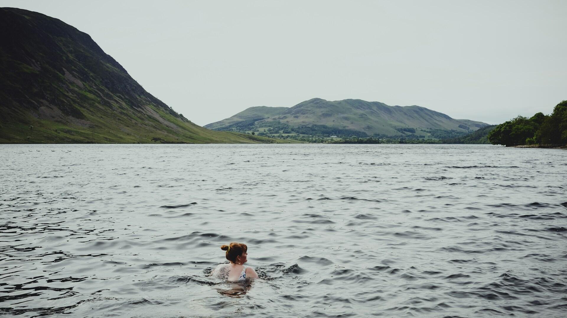Person svømmer i et stort vann med fjell i bakgrunnen.