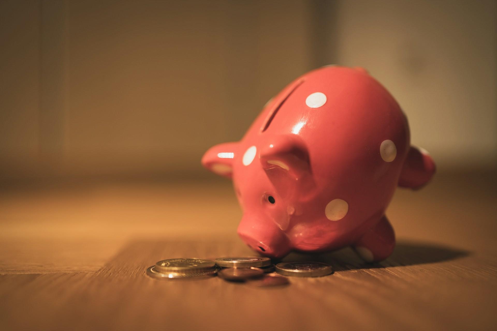 A piggy bank pointed downwards towards some coins.