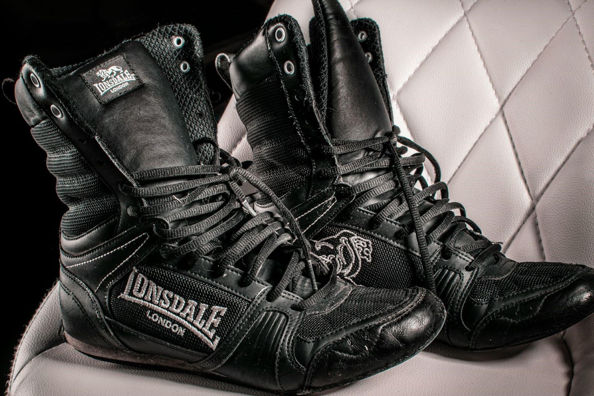 Pair of black high-top Lonsdale boxing boots resting on a white padded seat