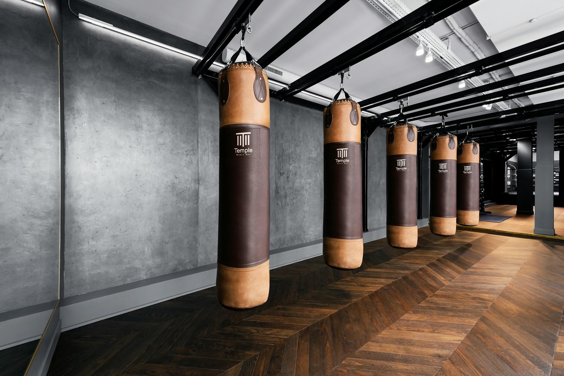 Five brown heavy bags hanging inside an empty boxing gym with wooden flooring