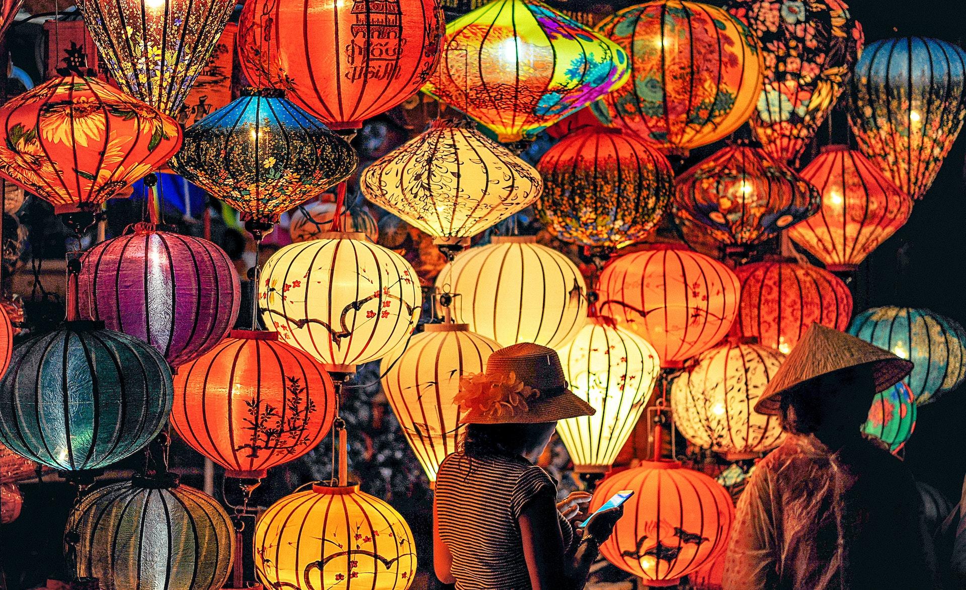 Two women stand in front of a large display of paper lanterns lit up at night.