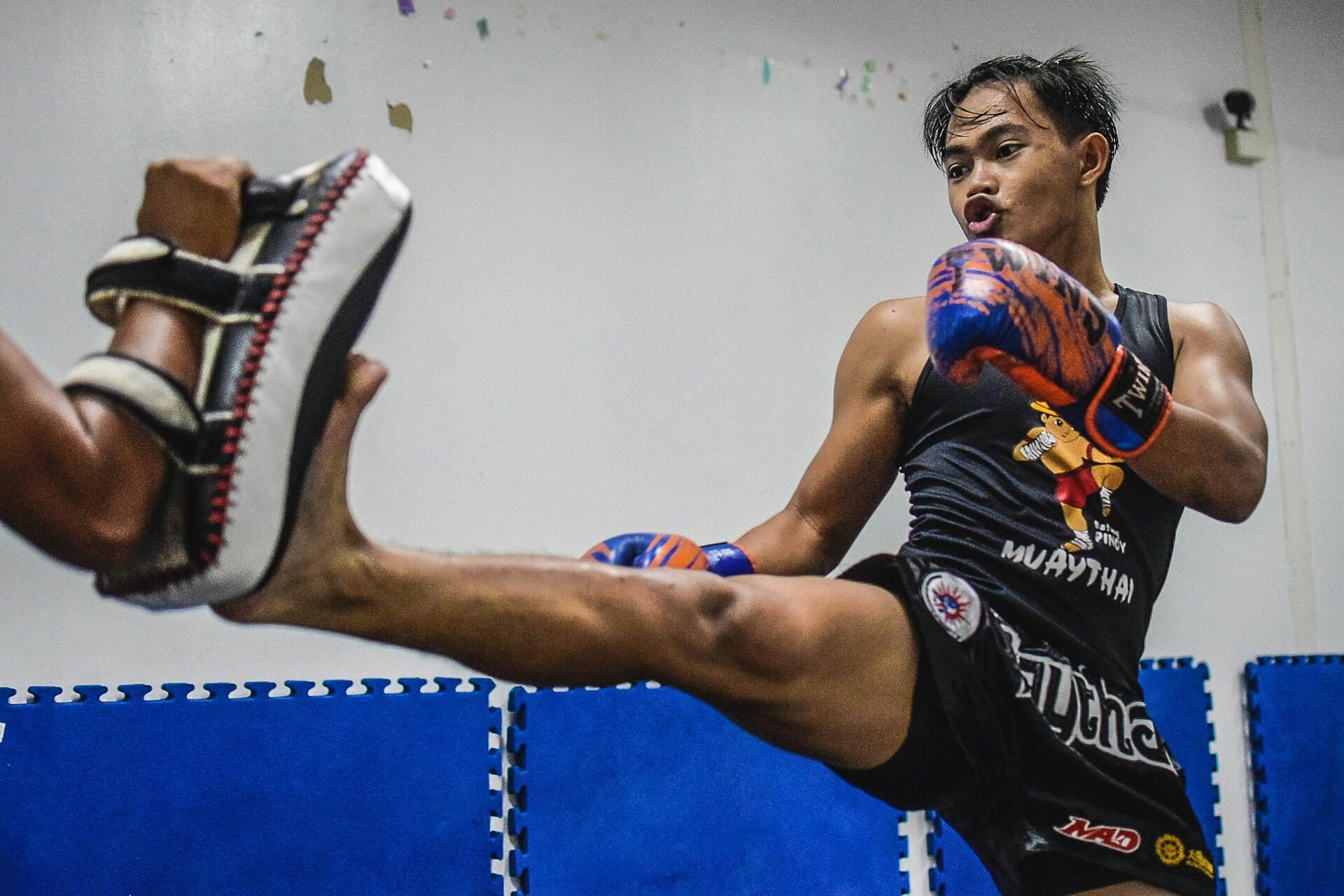 Muay Thai athlete wearing boxing gloves and kicking a handheld training pad