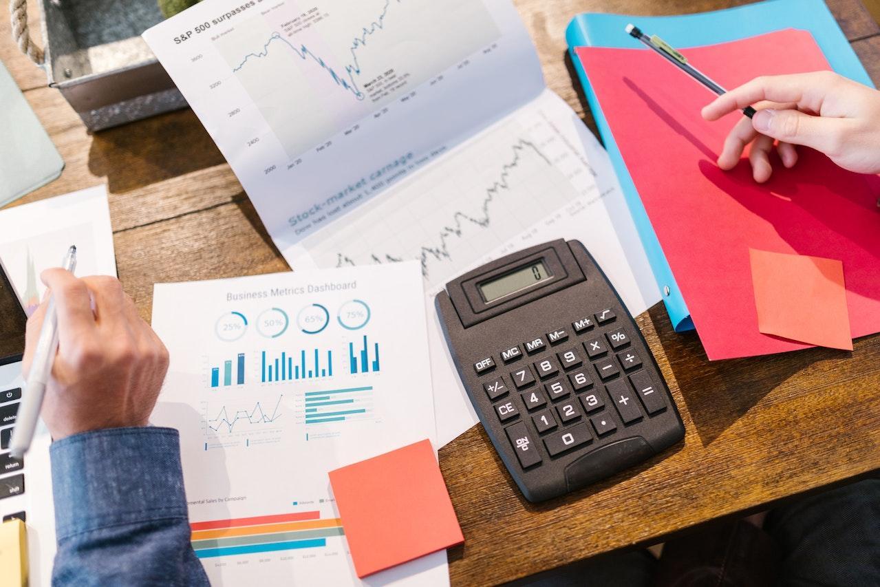 A calculator on top of a lot of papers showing graphs and financial data.