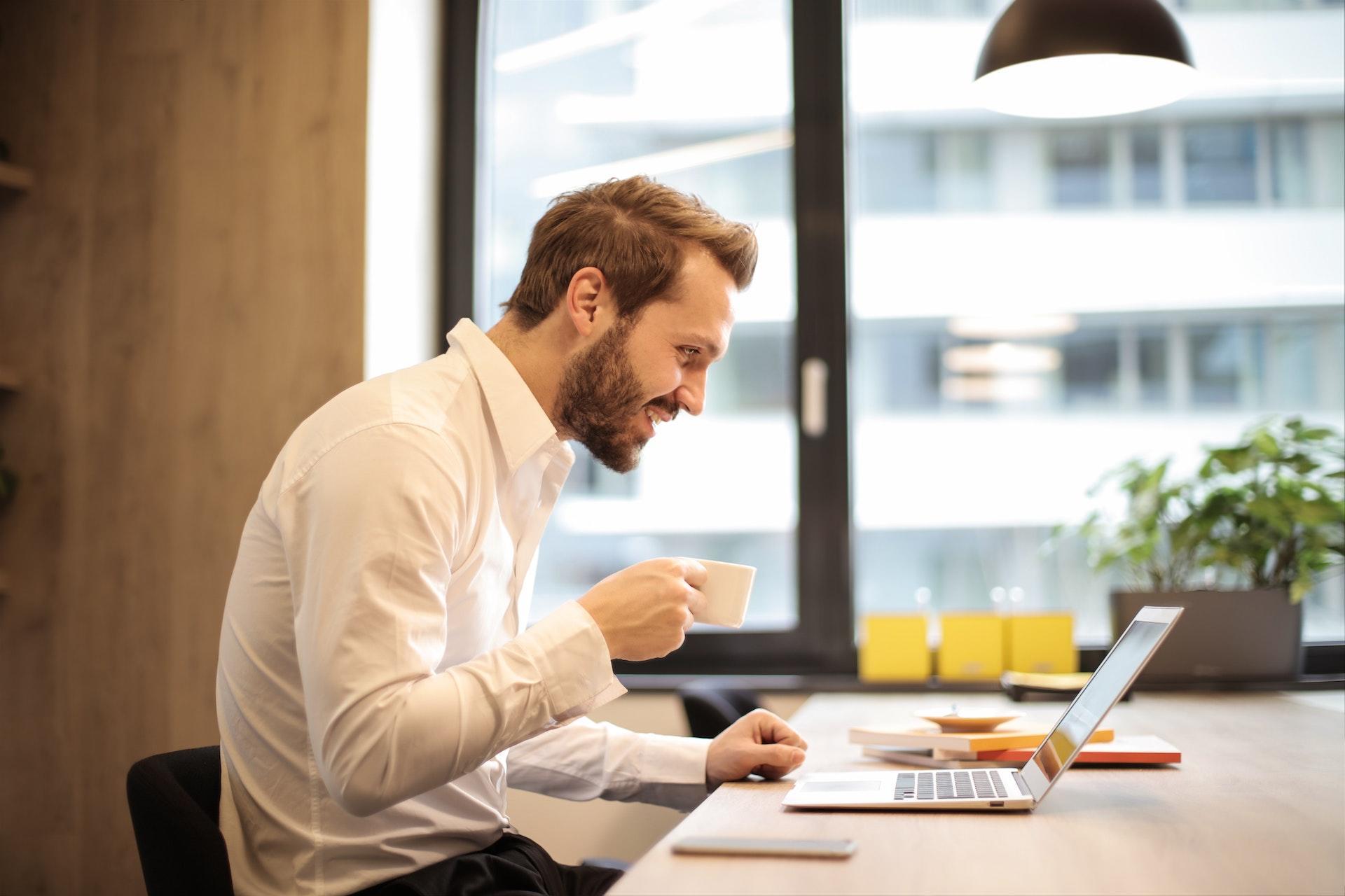 A person sitting at a desk looking at their computer and smiling.