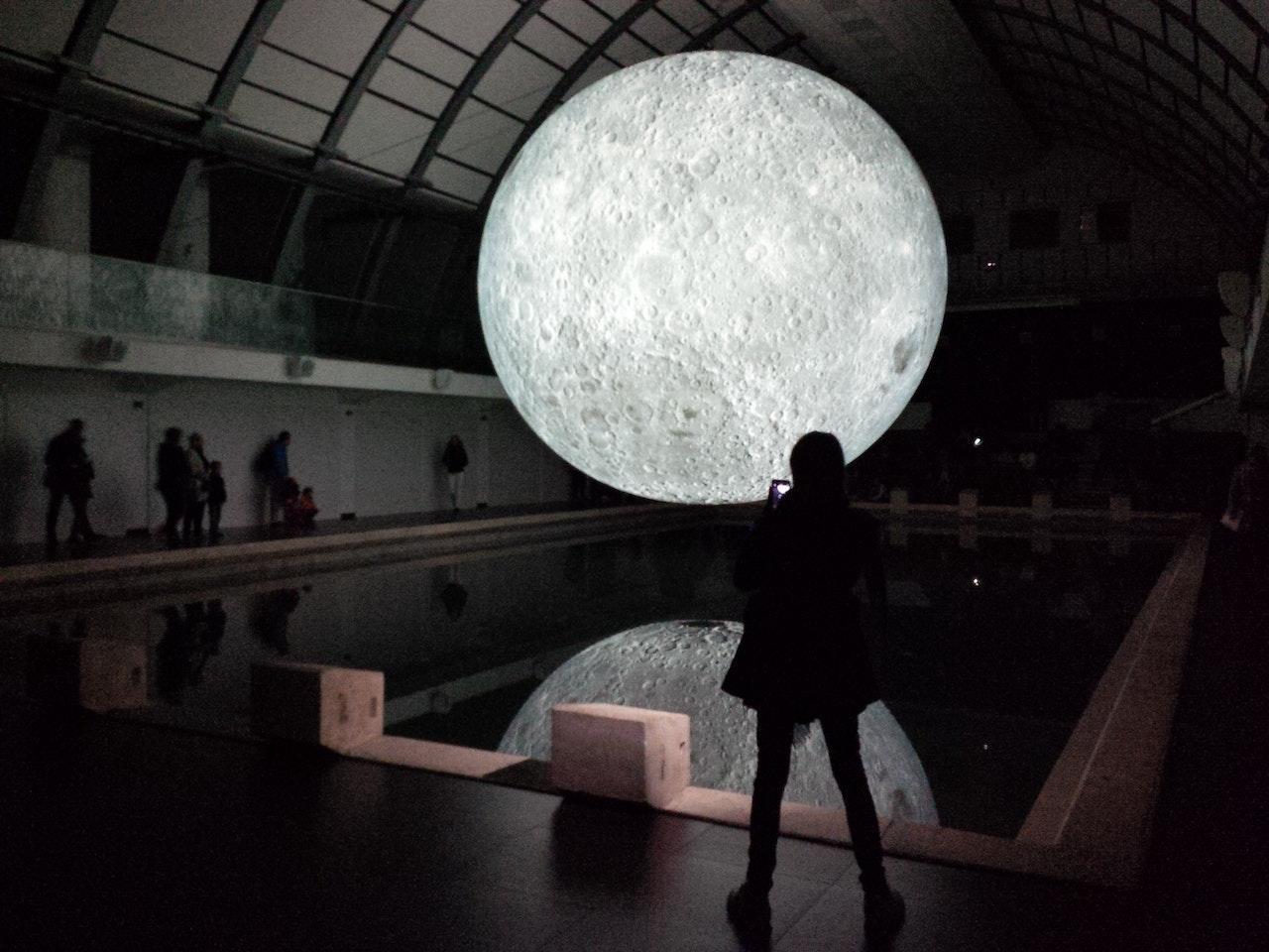 An art exhibit installation of a large, glowing moon in a dark room.