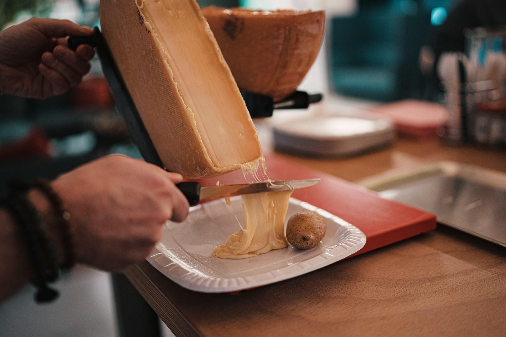 A person scraping raclette cheese onto a plate.