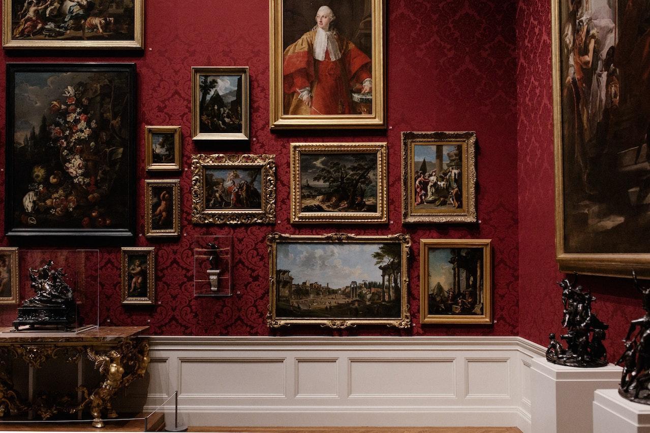 A wall of paintings in ornate frames in a museum.