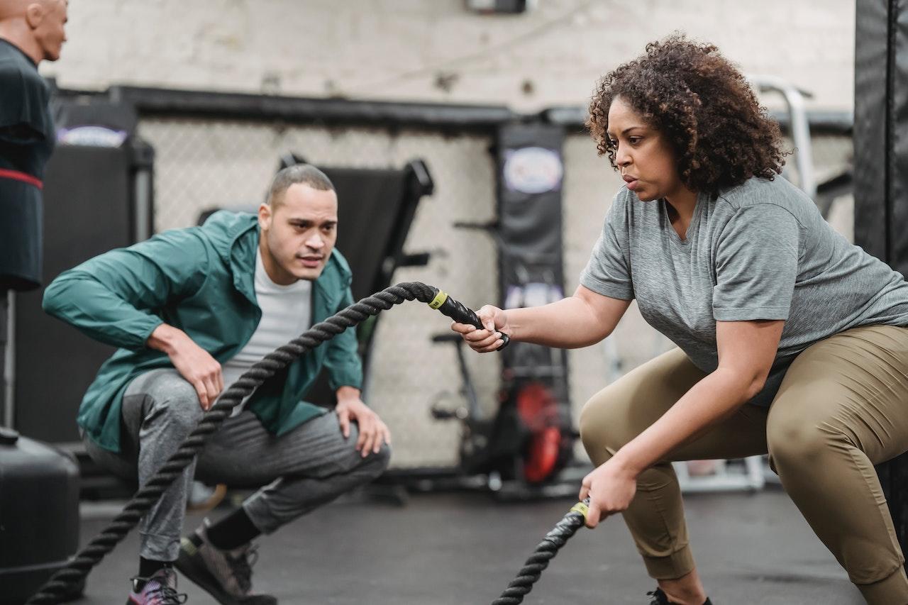 A personal trainer cheers on their student using battle ropes for fitness.