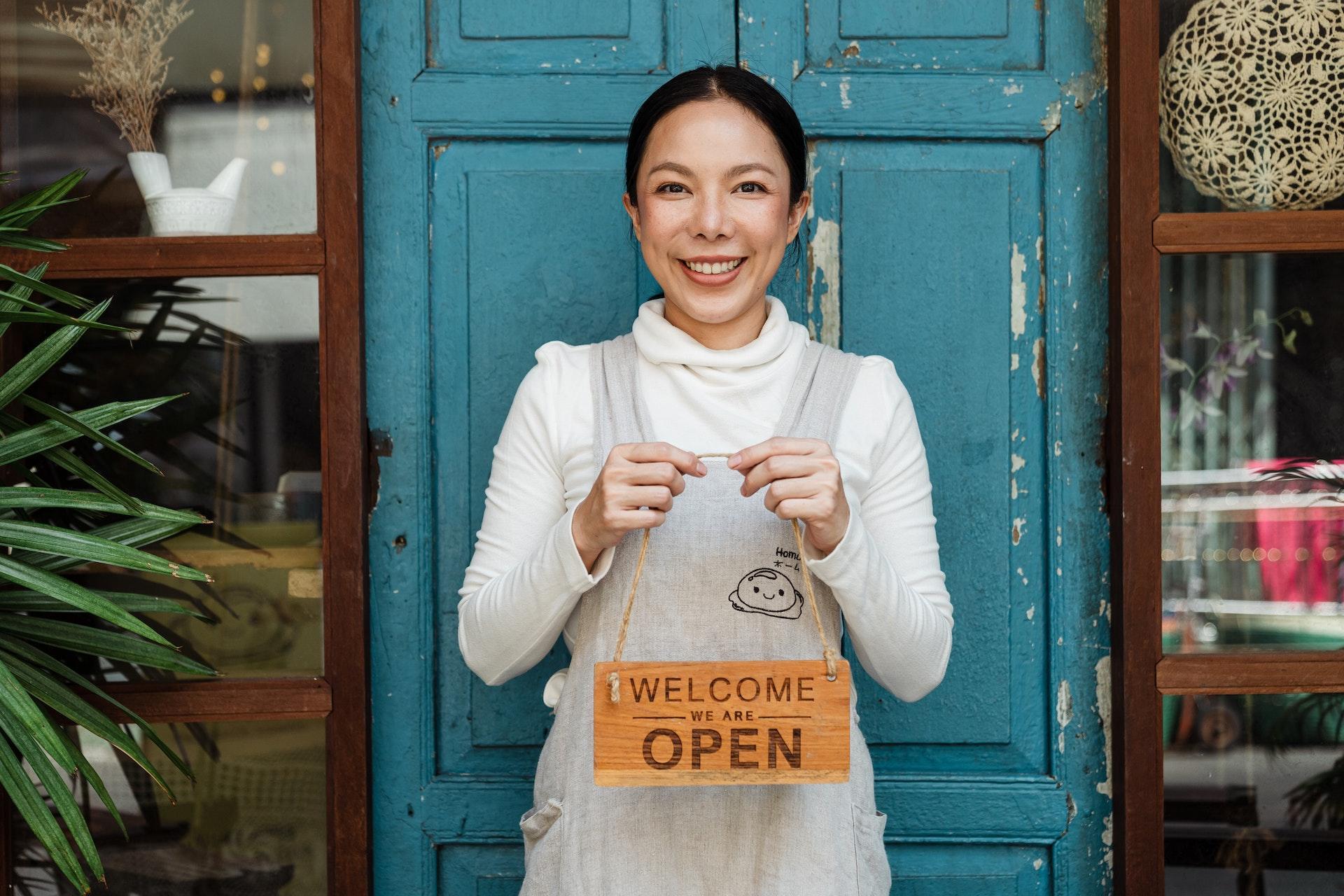A person stands in front of a blue door smiling and holding a sign that says