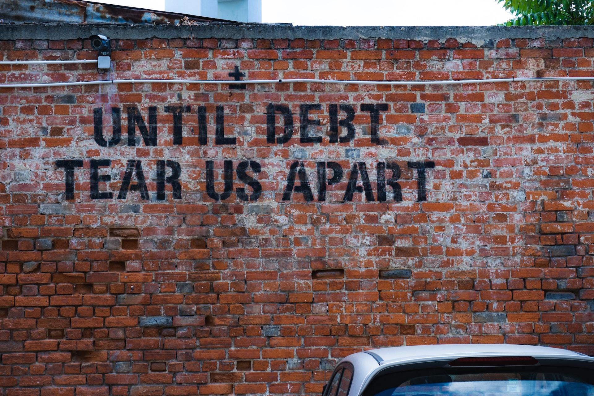 A wall with graffiti reading "Until debt tear us apart".