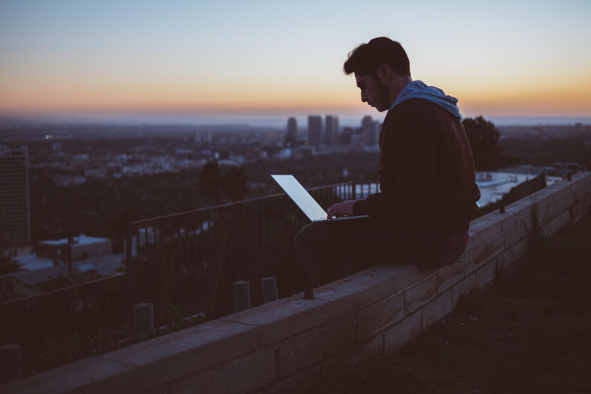 A man sitting on a wall with a laptop.