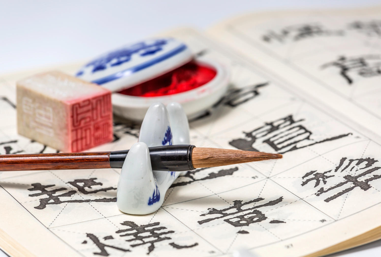 A close up of Chinese calligraphy and a calligraphy brush, as well as a seal and red ink