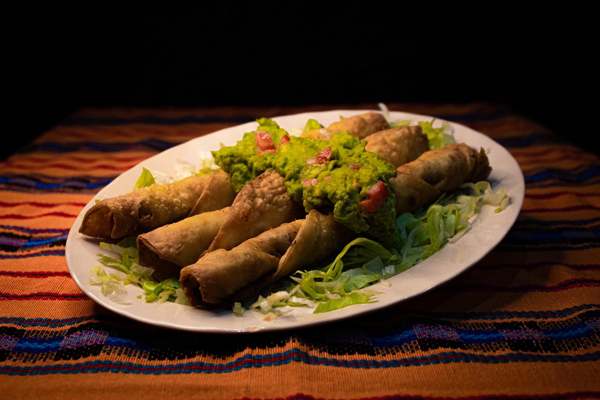 A plate of enchiladas with guacamole on top.