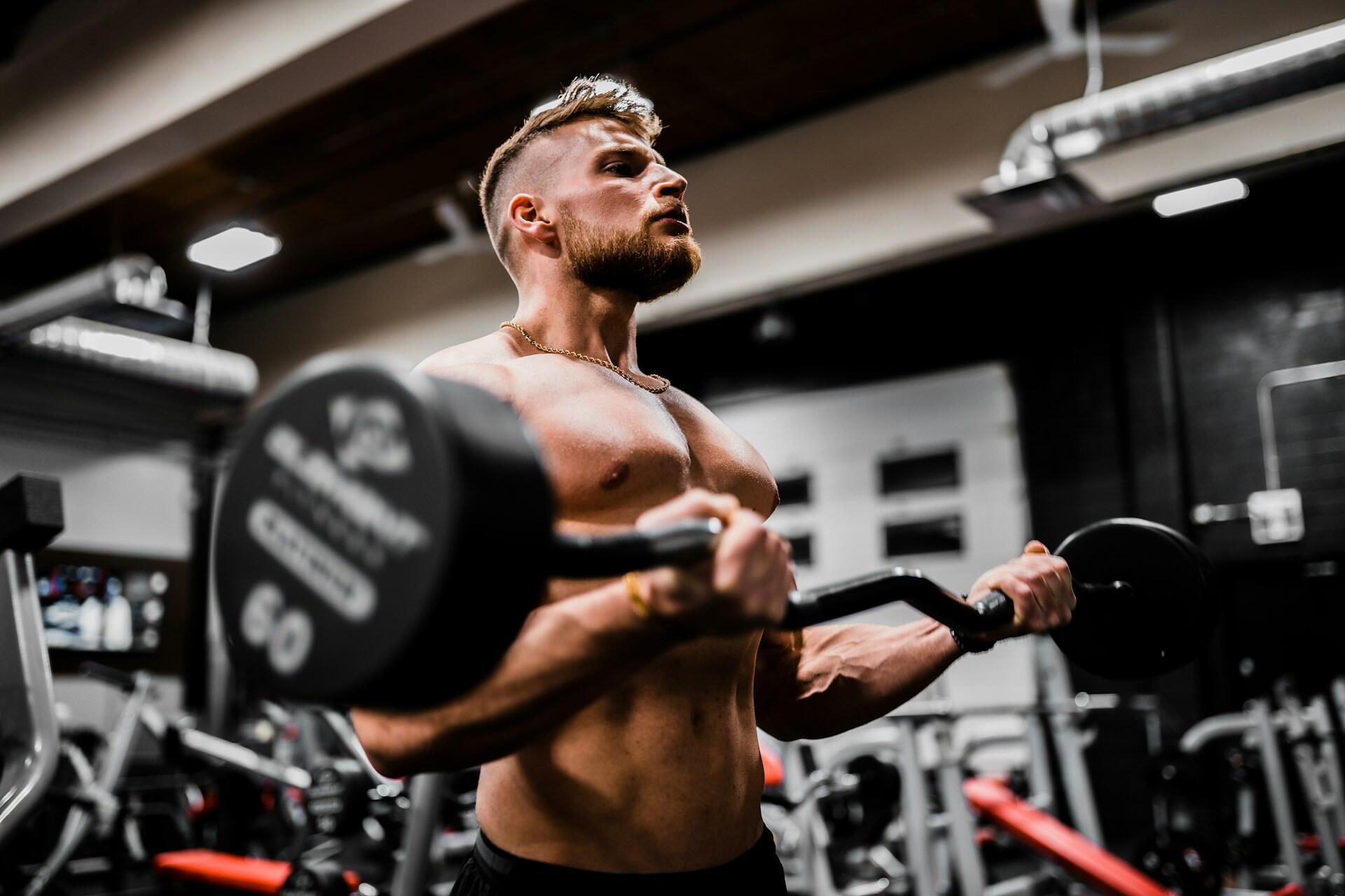 Man performing a curl with an EZ bar in a gym