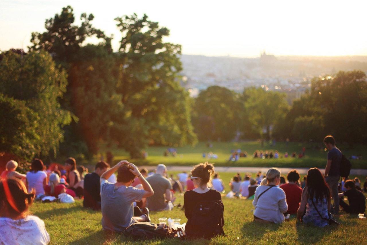 A large number of people sit in a grassy area outdoors on a nice day.