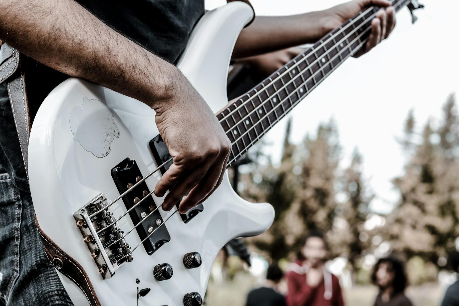person playing white bass guitar outdoors