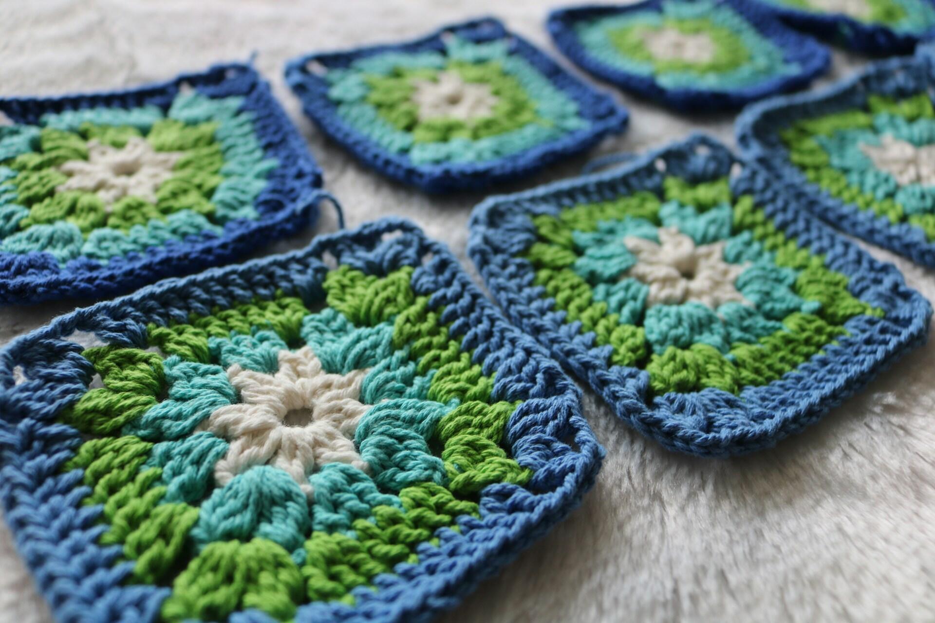 Blue, green and cream crocheted granny squares on a light fabric surface.
