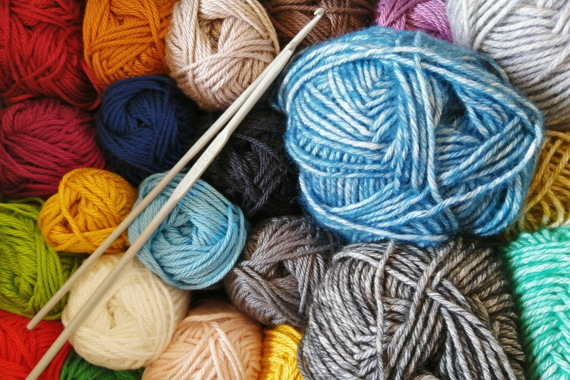 White crochet hooks lying on balls of yarn in red, blue, yellow, cream, grey and turquoise.