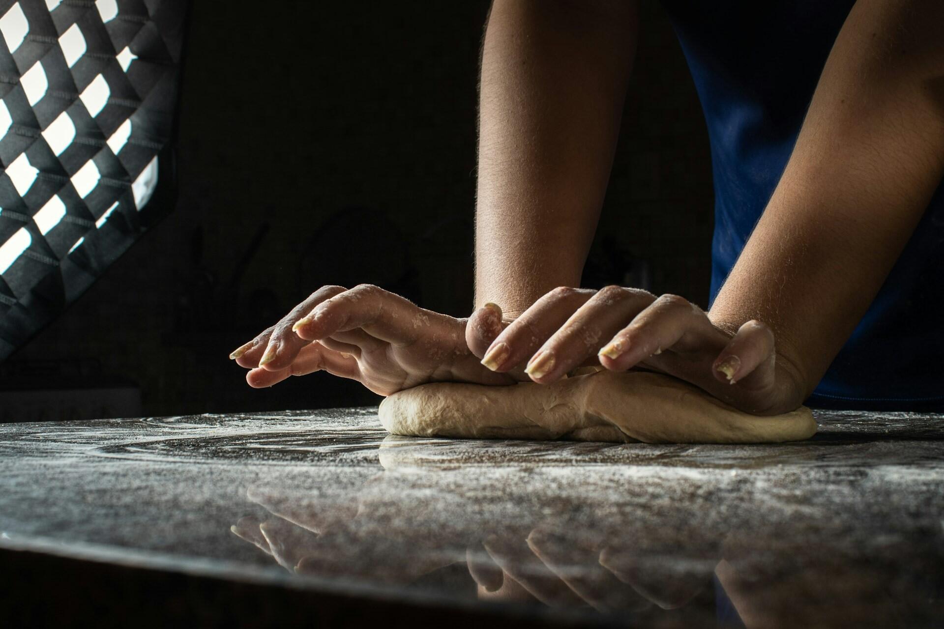 A pair of hands kneads dough on a floured countertop, with soft lighting highlighting the baking process.