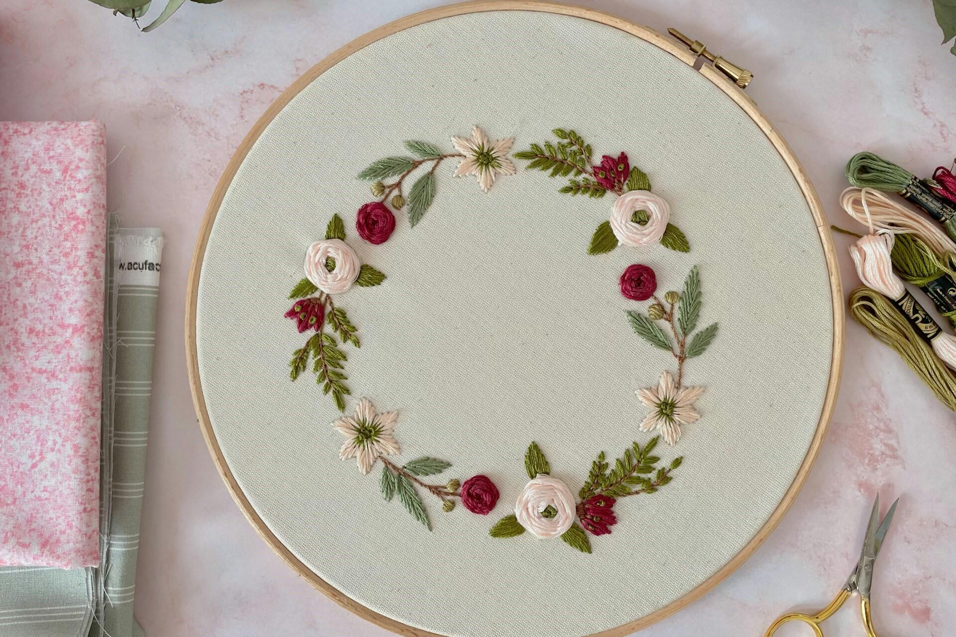 Floral embroidery in a wooden hoop with thread, scissors and folded fabric nearby