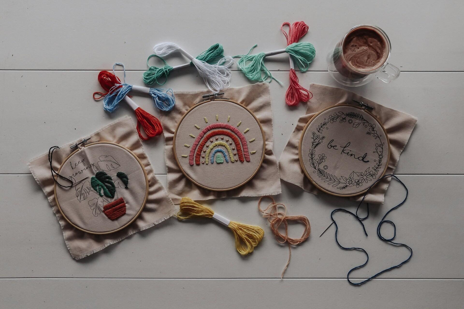 Embroidery hoops with fabric designs, coloured thread and a cup on a table