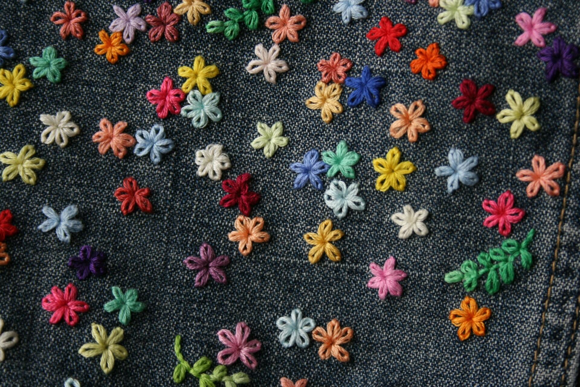 Colourful embroidered flowers stitched onto dark denim fabric