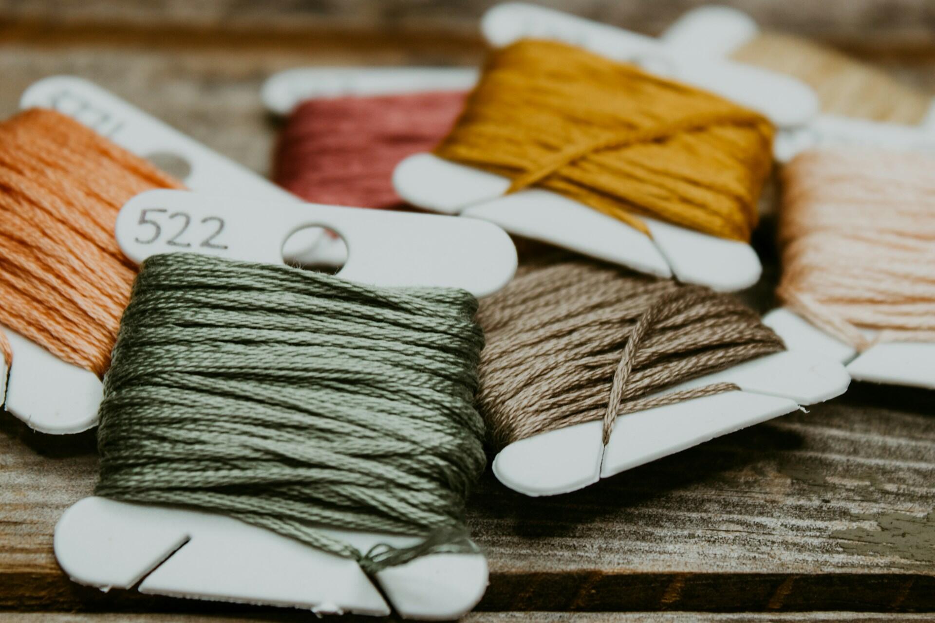 Embroidery thread wrapped around white bobbins on a wooden surface
