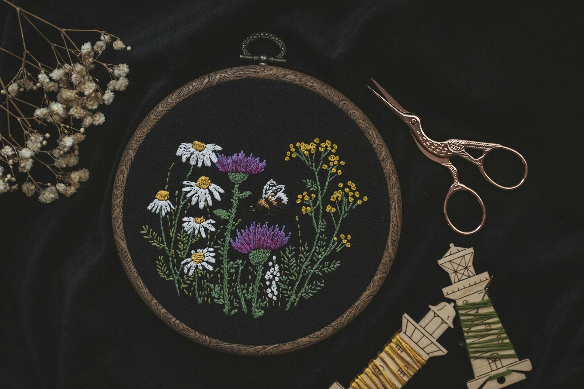 Floral embroidery in a hoop with scissors and thread on a dark surface