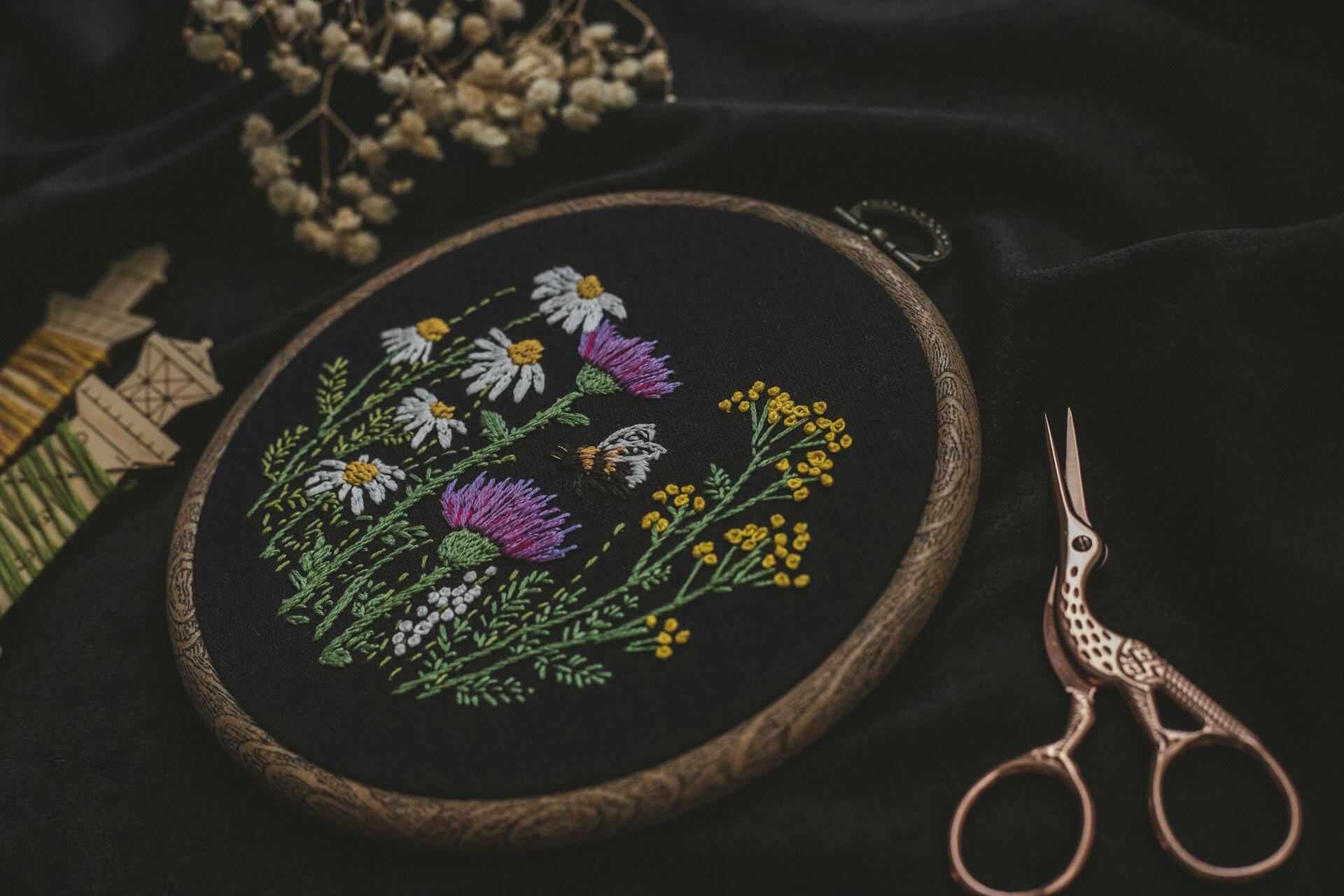 Floral embroidery in a wooden hoop beside decorative scissors on dark fabric