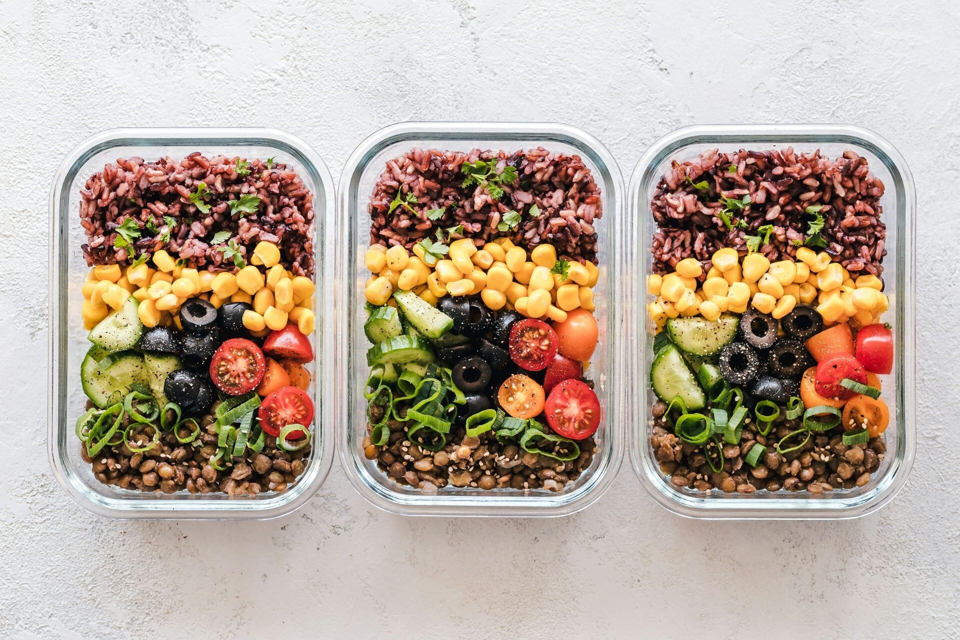 Three glass meal-prep containers filled with rice, lentils, corn and vegetables
