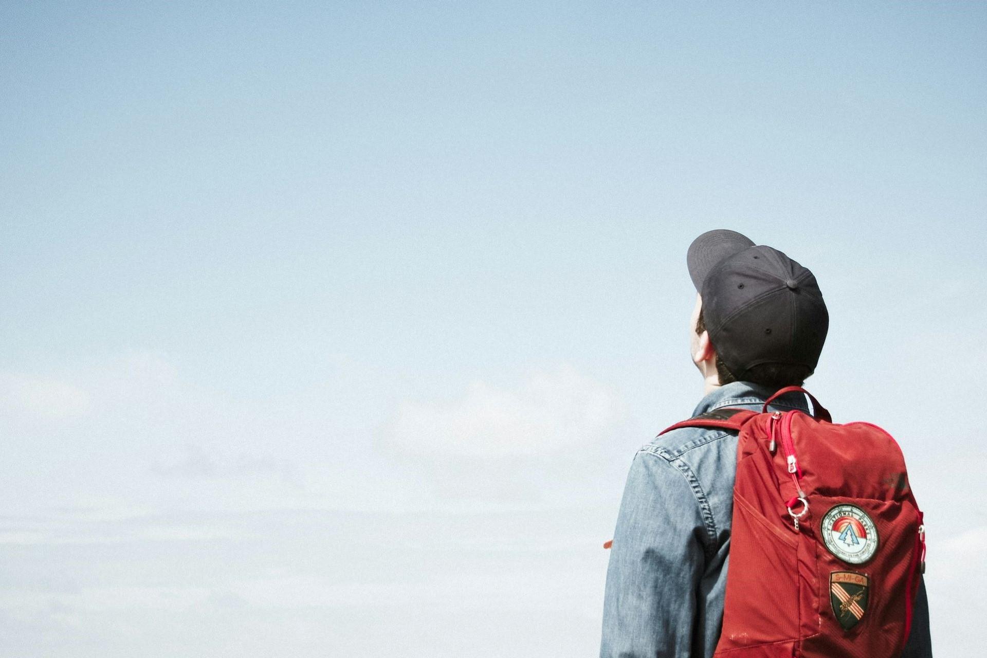 A person with a backpack and cap staring into the sky.