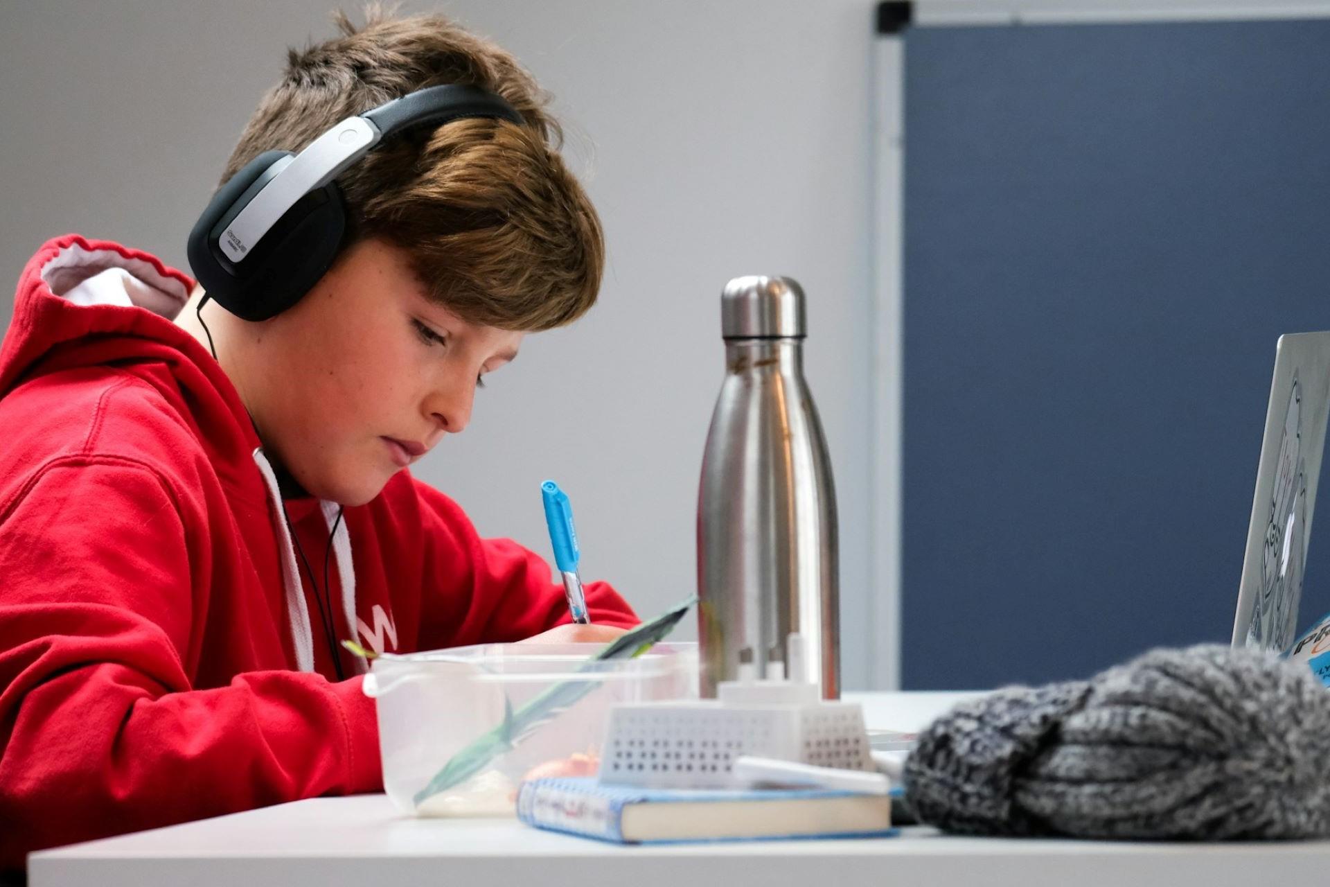 A child with headphones on studying in front of a laptop.