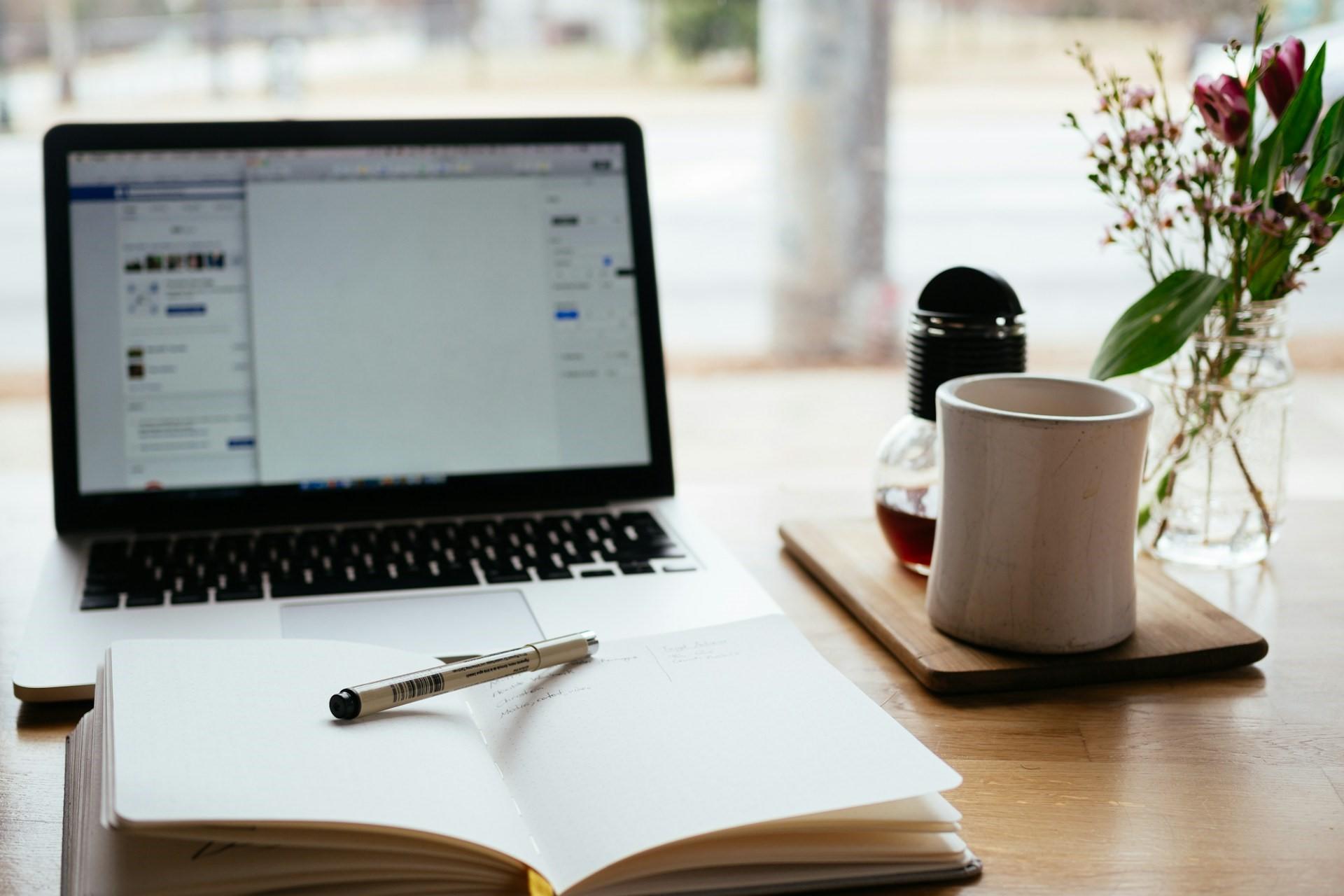 A laptop, notebook, and coffee cup.