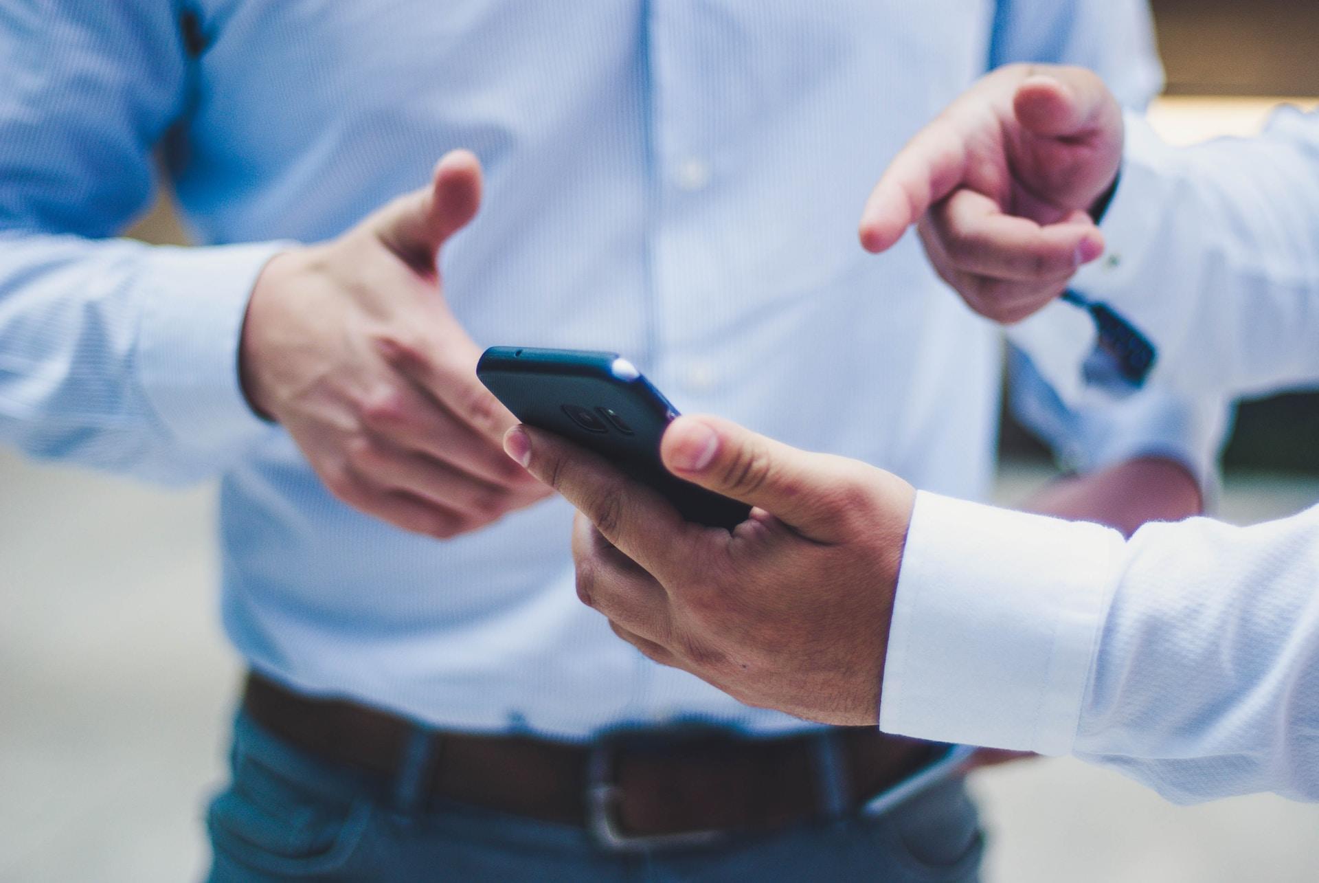 Two men in shirts pointing at a smart phone.