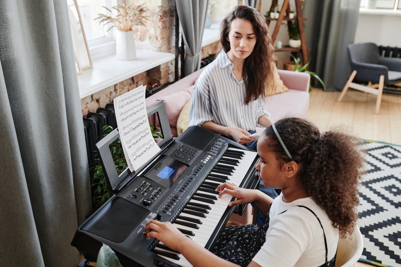 A piano teacher observes her student playing at the keyboard.