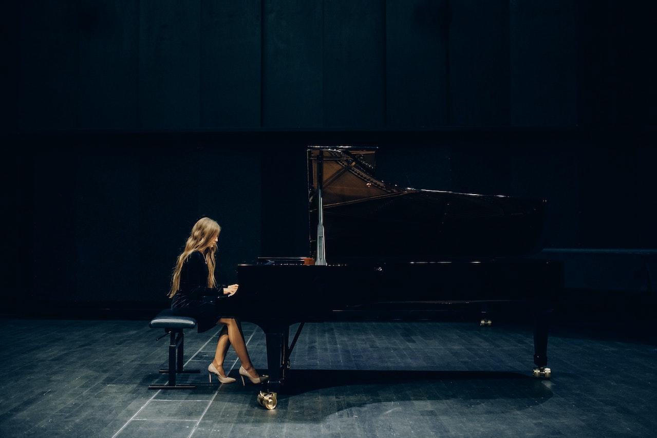 A pianist woman in a black dress sits at a grand piano on stage.