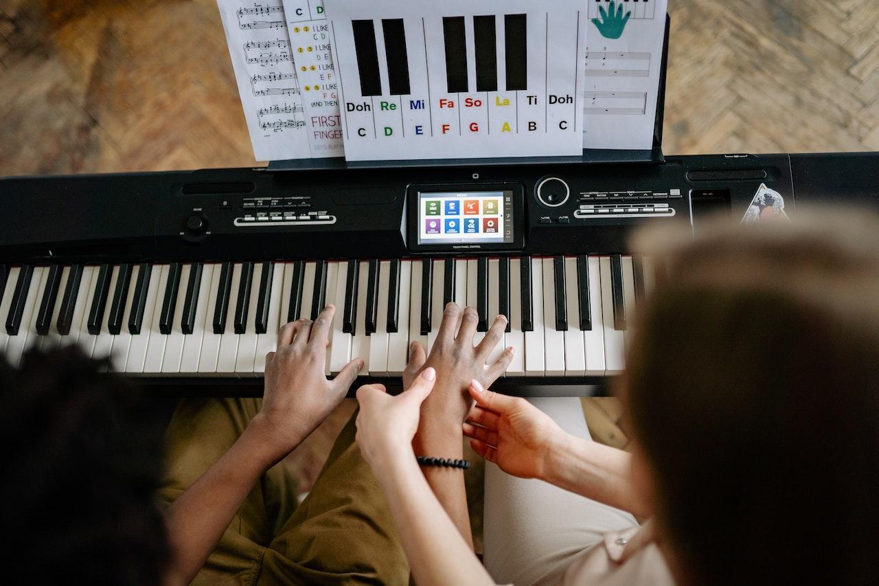 An overhead view of a piano teacher positioning the student's hands on the keys.