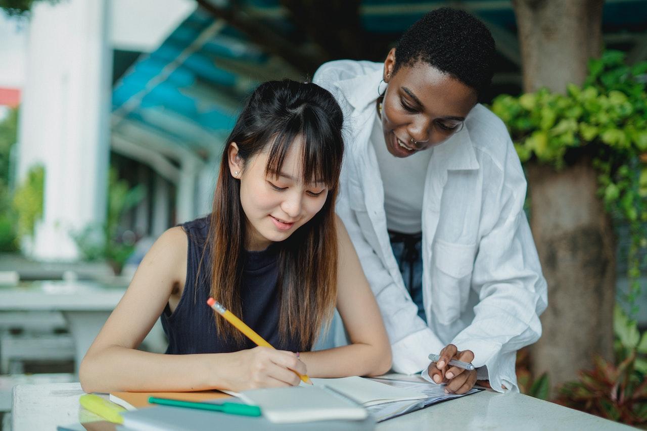 A student writing in a notebook is assisted by her tutor.