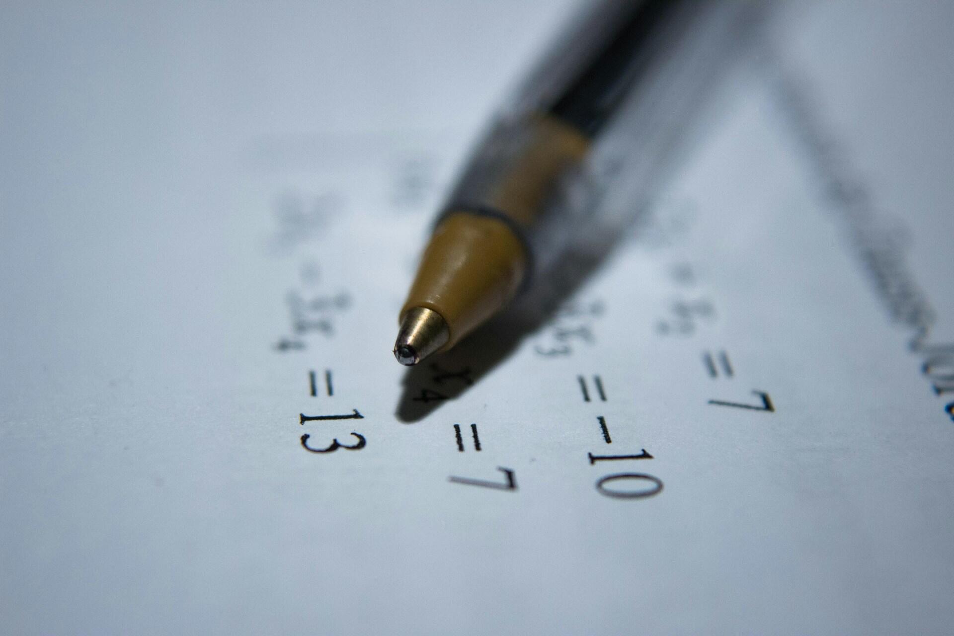 Pen resting on a maths worksheet with simple equations